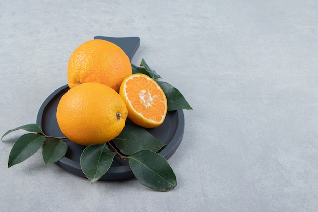 Fresh oranges with leaves on black cutting board