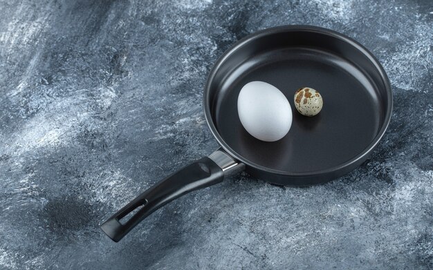 Fresh organic chicken and quail eggs in black frying pan.