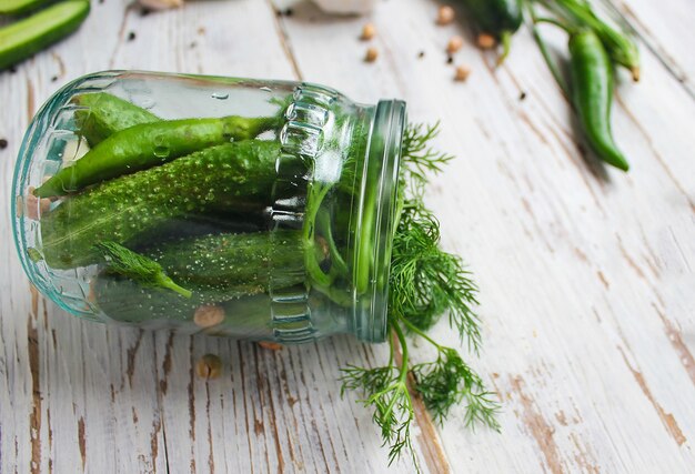 Fresh organic cucumbers pickles jar on white wooden table with green and red and chili peppers, fennel, salt, black peppercorns, garlic, pea, green tomatoes, close up, healthy concept, top view, flat lay