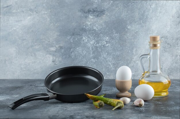 Fresh organic eggs with pepper and oil over grey background