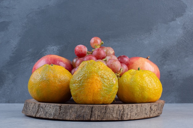 Free photo fresh organic fruits on wooden board. tangerine, red grape and apple.