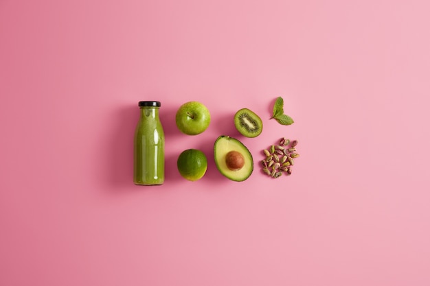 Fresh organic green smoothie and ingredients apple lime, half of avocado, pistachio and mint leaf on pink background. Non alcoholic nutrient vegetarian beverage. Natural detox food. Dieting concept