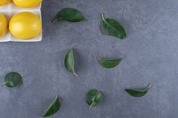 Fresh organic lemons and leaves over grey background.