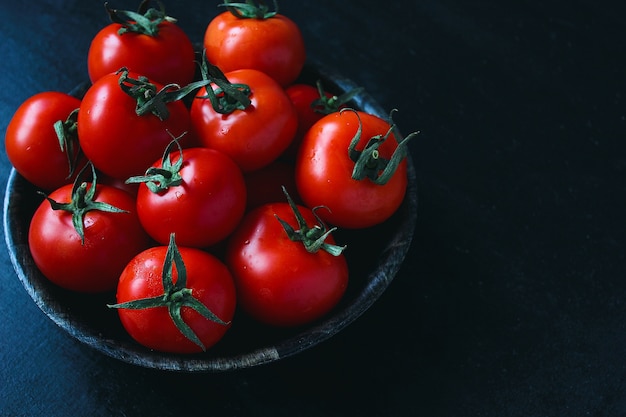 Fresh organic red tomatoes in black plate, close up, healthy concept, top view