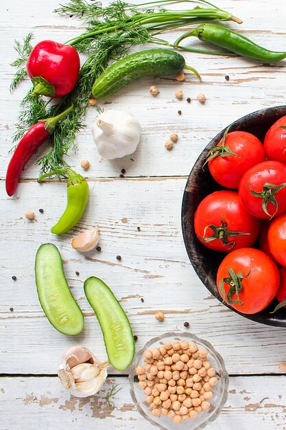 Fresh organic red tomatoes in black plate on white wooden table with green and red and chili peppers, green peppers, black peppercorns, salt, close up, healthy concept