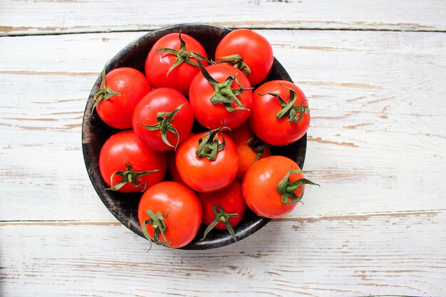 緑と赤と唐辛子、ピーマン、黒胡pepper、塩、クローズアップ、健康的な概念と白い木製テーブルの上の黒い皿に新鮮な有機赤いトマト