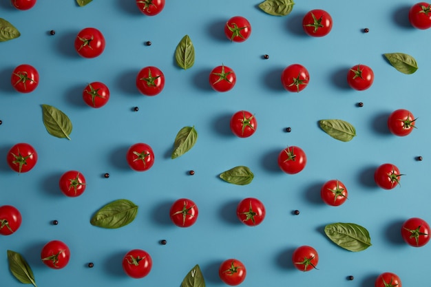 Свежие органические красные помидоры, перец горошком и листья базилика на синем фоне. Заготовленные овощи для приготовления салата. Концепция здорового питания и витаминов. Горизонтальный снимок, вид сверху. Вкусная натуральная еда