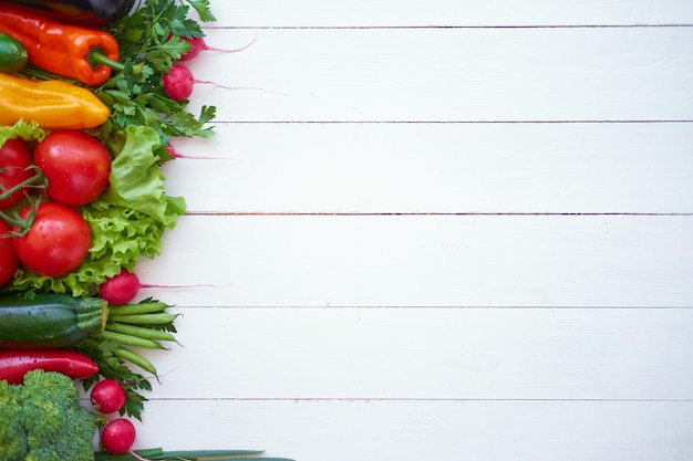 Fresh organic vegetables on white wooden boards background, top view. Healthy food concept.