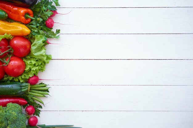 Fresh organic vegetables on white wooden boards background, top view. Healthy food concept.