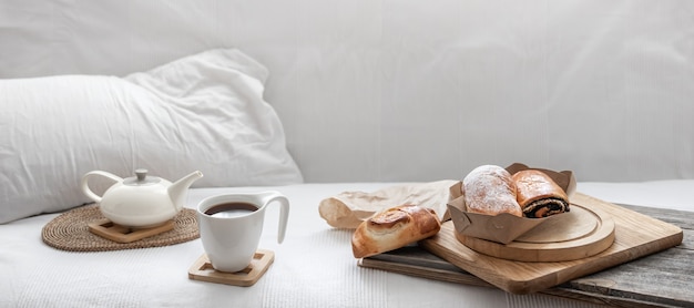 Fresh pastries and a cup of coffee on the background of a white bed. Brunch and weekend concept.