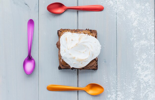 Fresh pastry with multi colored spoons on wooden background
