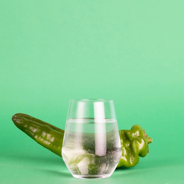 緑の背景に新鮮な唐辛子と水のガラス