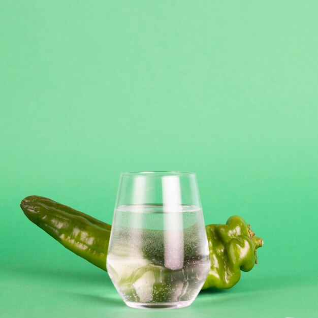 Свежий перец и стакан воды на зеленом фоне