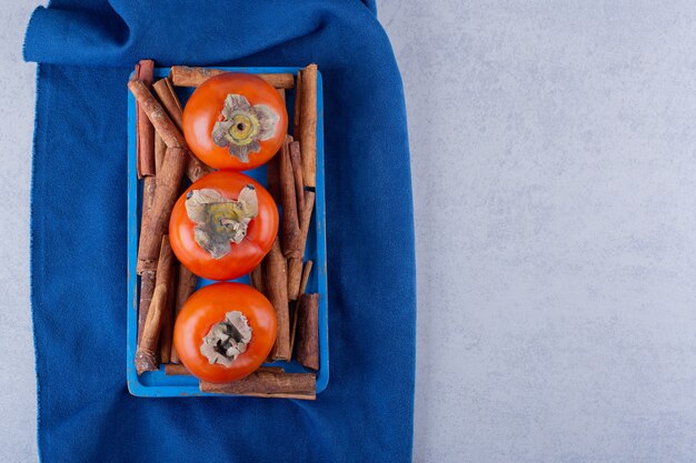 Свежие фрукты хурмы и палочки корицы на синей тарелке.