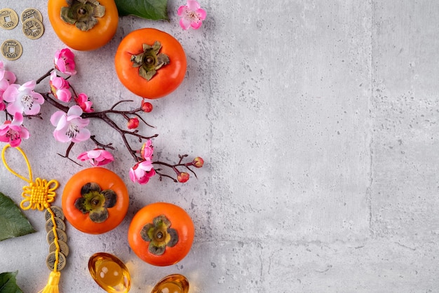 中国​の​旧​正月​の​果物​の​デザイン​の​灰色​の​テーブル​の​背景​に​新鮮な​柿​、​黄金​の​コイン​の​言葉​は​それ​が​作った​王朝​の​名前​を​意味します​。