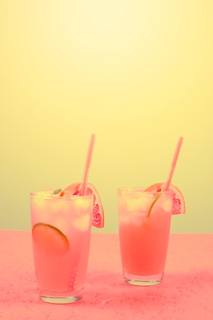Свежий розовый алкогольный коктейль с грейпфрутом; ломтик лимона и кубики льда на желтом фоне
