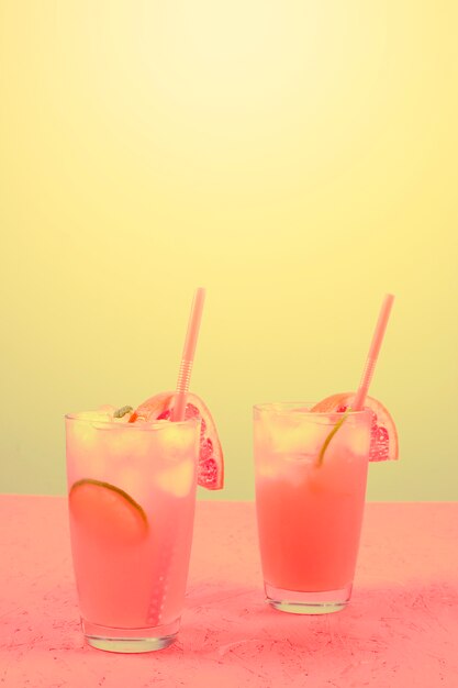 Fresh pink alcoholic cocktail with grapefruit; lemon slice and ice cubes against yellow background