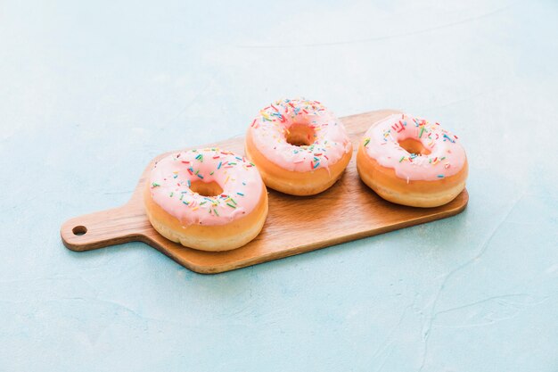 Fresh pink donuts on wooden chopping board