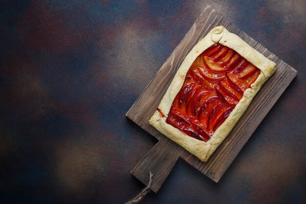 Fresh plum galette pie with raw plums on dark 