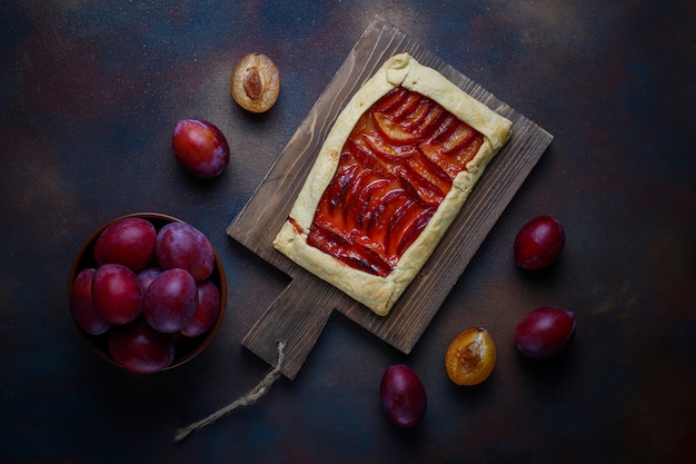 Fresh plum galette pie with raw plums on dark 