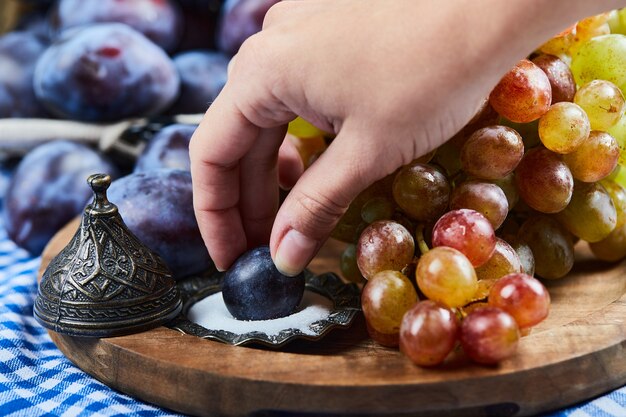 Fresh plums, a bunch of grapes and salt on a wooden board. 