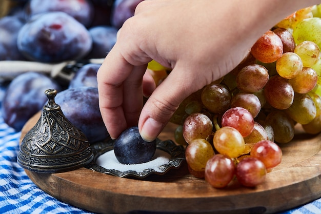 Свежие сливы, гроздь винограда и соль на деревянной доске.