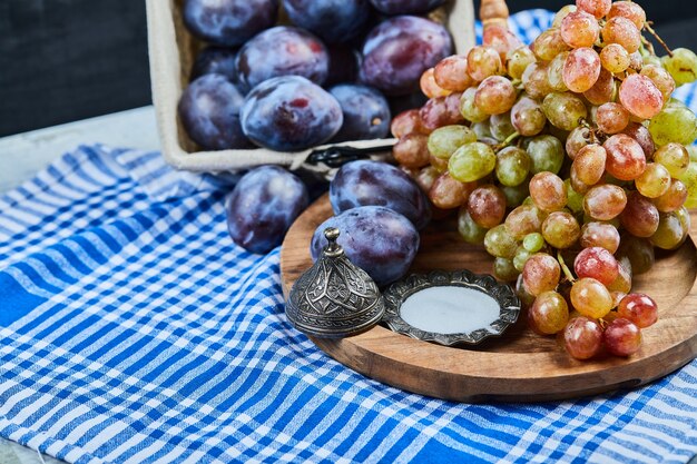 Fresh plums and a bunch of grapes on tablecloth.