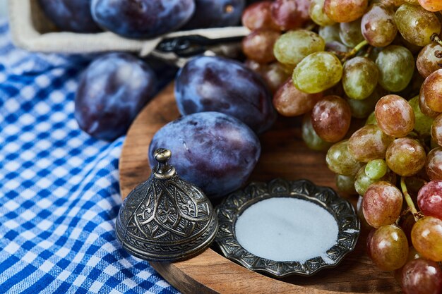 Fresh plums and a bunch of grapes on wooden plate.