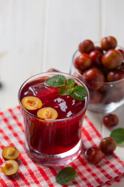 Fresh plums juice on the white wooden surface.