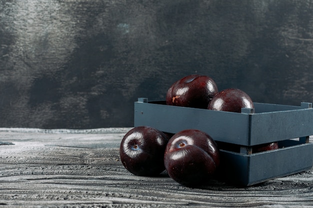 Fresh plums in a plate on a dark grey background. side view.