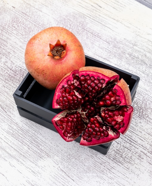 Free photo fresh pomegranate in black basket on white wooden table