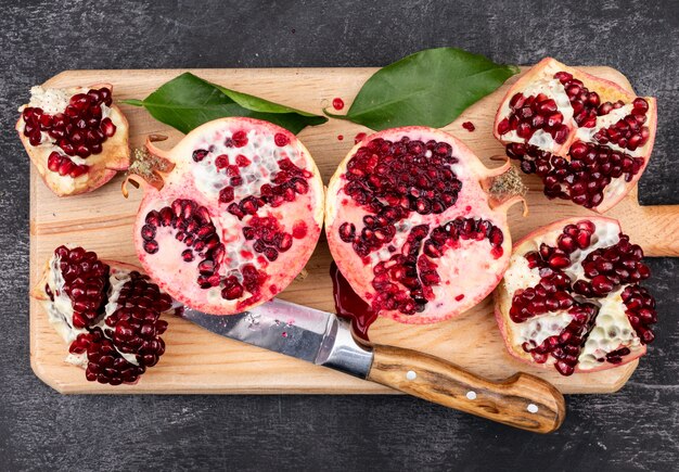 fresh pomegranates with knife top view on wooden cutting board on dark
