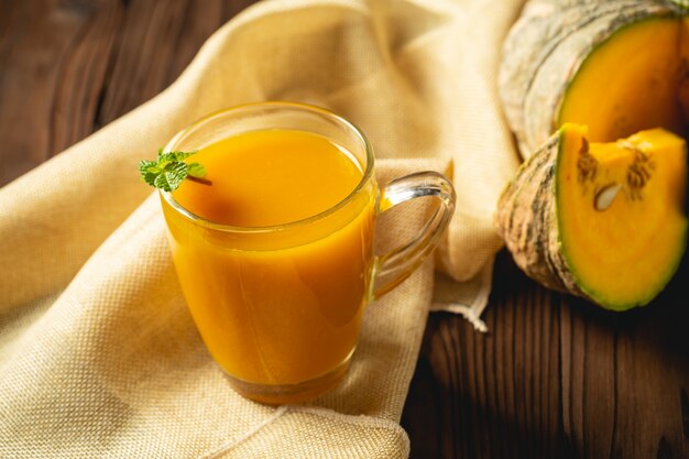 Fresh pumpkin juice in glass on wooden table.