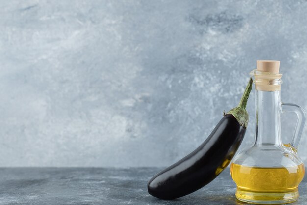 Fresh purple eggplant with oil on grey background.