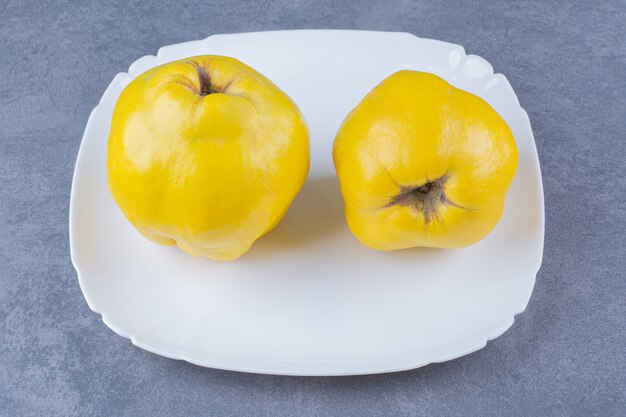 Fresh quince fruits on plate on marble table.