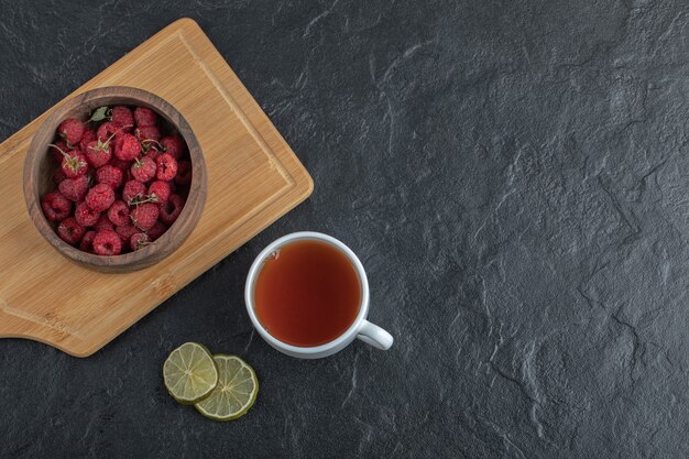 Fresh raspberries on wooden board with tea and lemon. 
