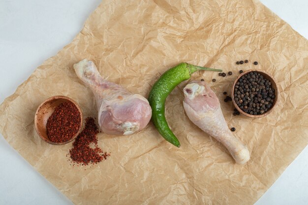 Fresh raw chicken legs with spices on food paper.