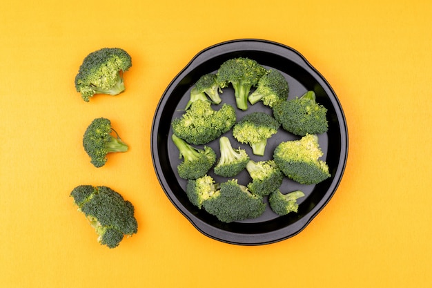 Fresh raw green broccoli in a frying pan on yellow surface