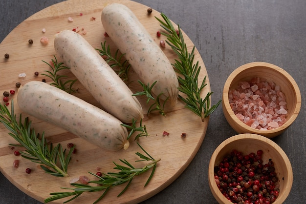 Free photo fresh raw sausages and ingredients for cooking. classic boiled meat pork sausages on chopping board with pepper, rosemary, herbs and spices.