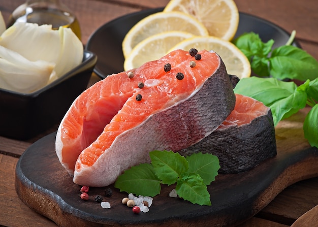 Fresh and raw steaks trout on a wooden cutting board with sliced lemon, rosemary and pepper