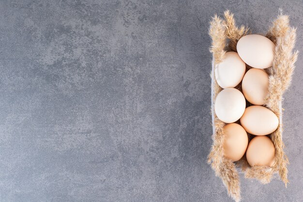 Fresh raw white chicken eggs with wheat ears placed on stone table .