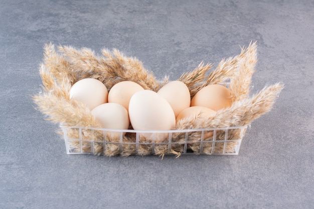 石のテーブルに置かれた小麦の穂を持つ新鮮な生の白い鶏の卵。