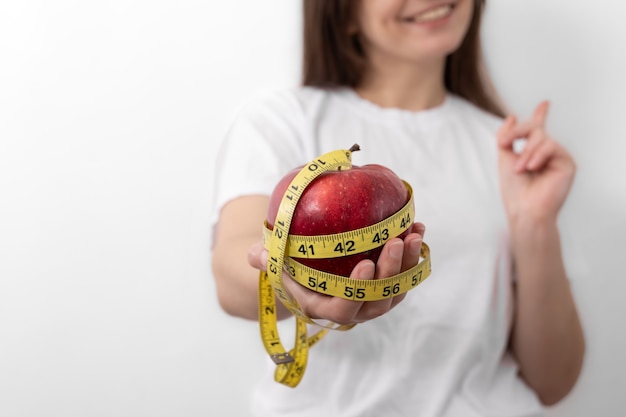 Fresh red apple with a measuring tape in female hands closeup