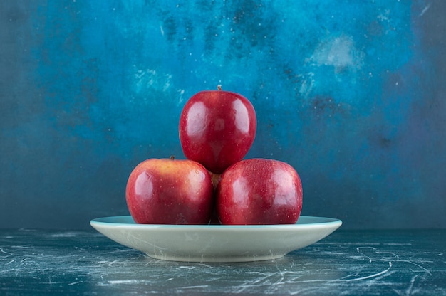Свежие красные яблоки на синей тарелке.