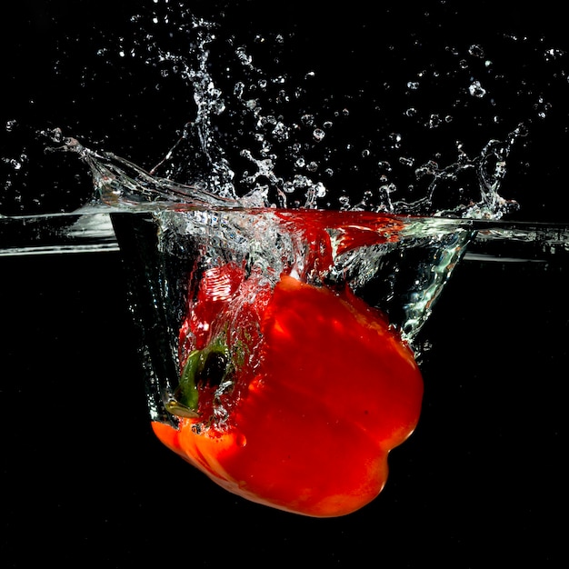 Fresh red bell pepper falling in water with splash on black background