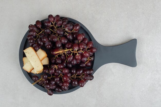 Fresh red grapes and cheese slices on dark board
