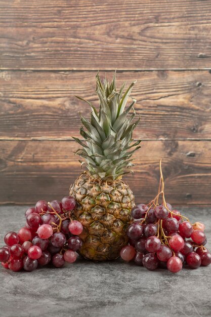 Fresh red grapes with ripe pineapple on marble surface.