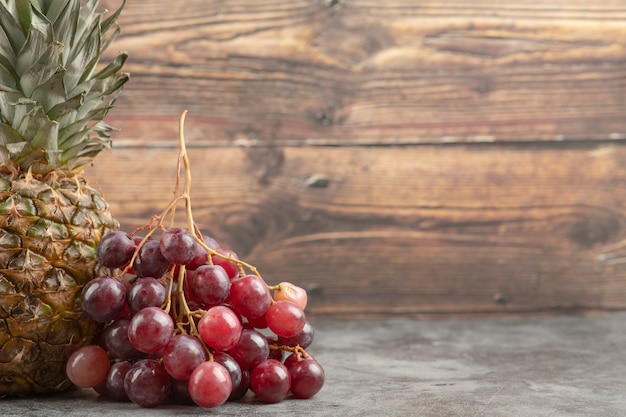 Fresh red grapes with ripe pineapple on marble surface.