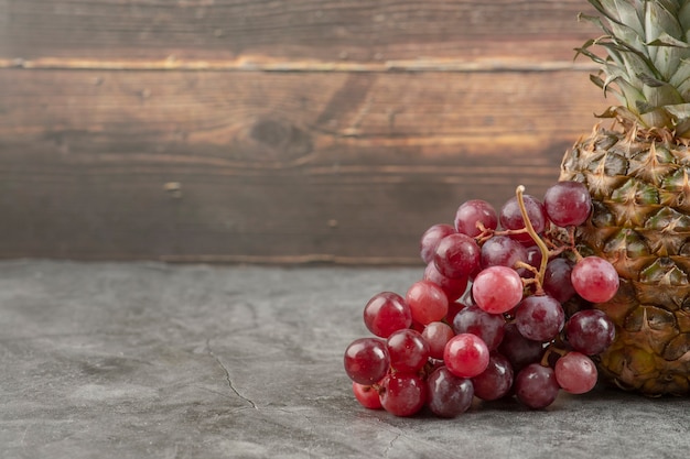 Fresh red grapes with ripe pineapple on marble surface.