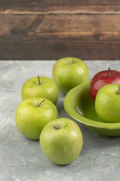 Fresh red and green apples in green bowl on marble.